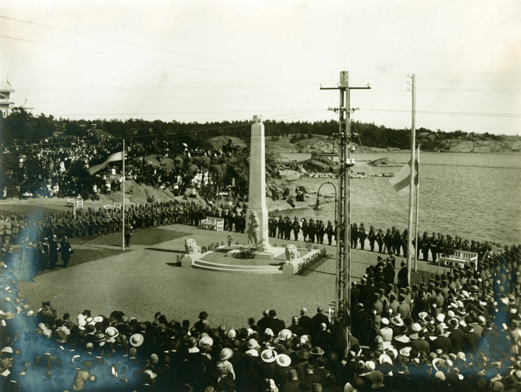 Vapauspatsaan vihkimistilaisuus. Suuri väkijoukko sekä patsaan luona että kallioilla. Frihetsstatyn invigs. Den stor samling människor både kring statyn och på klpiporna. The Freedom monument is revealed. A crowd has gathered around the statue and on the cliffs.