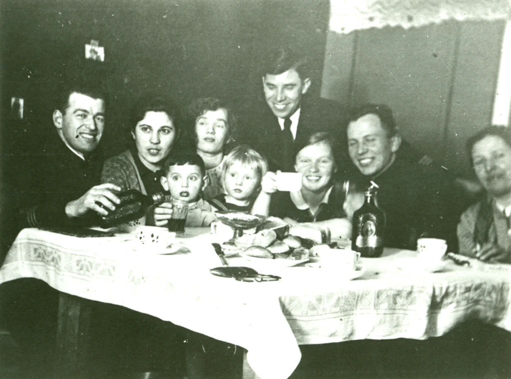 Venäläinen perhe pöydän ympärillä Hangossa 1940-luvulla. Pöydällä on leipiä, pulloja ja kahvikuppeja. Seurueessa on sekä aikuisia että lapsia. En rysk familj kring ett bord i Hangö på 1940-talet. På bordet står bröd, flaskor och kaffekoppar. I sällskapet ingår både vuxna och barn. A russian family sits by a table in Hanko in the 1940s. On the table are bread, bottles and coffe cups. There are both children and adults on the picture.