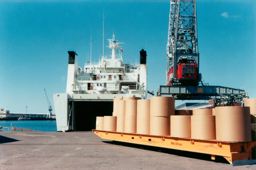 Hangon satama, jossa lasti paperirullia odottavat siirtoa sisään laivaan. Hangö hamn där en last med stora pappersrullar väntar på att bi förflyttade in i ett fartyg. The port of Hanko, where big paper rolls are about to be loaded into a boat.