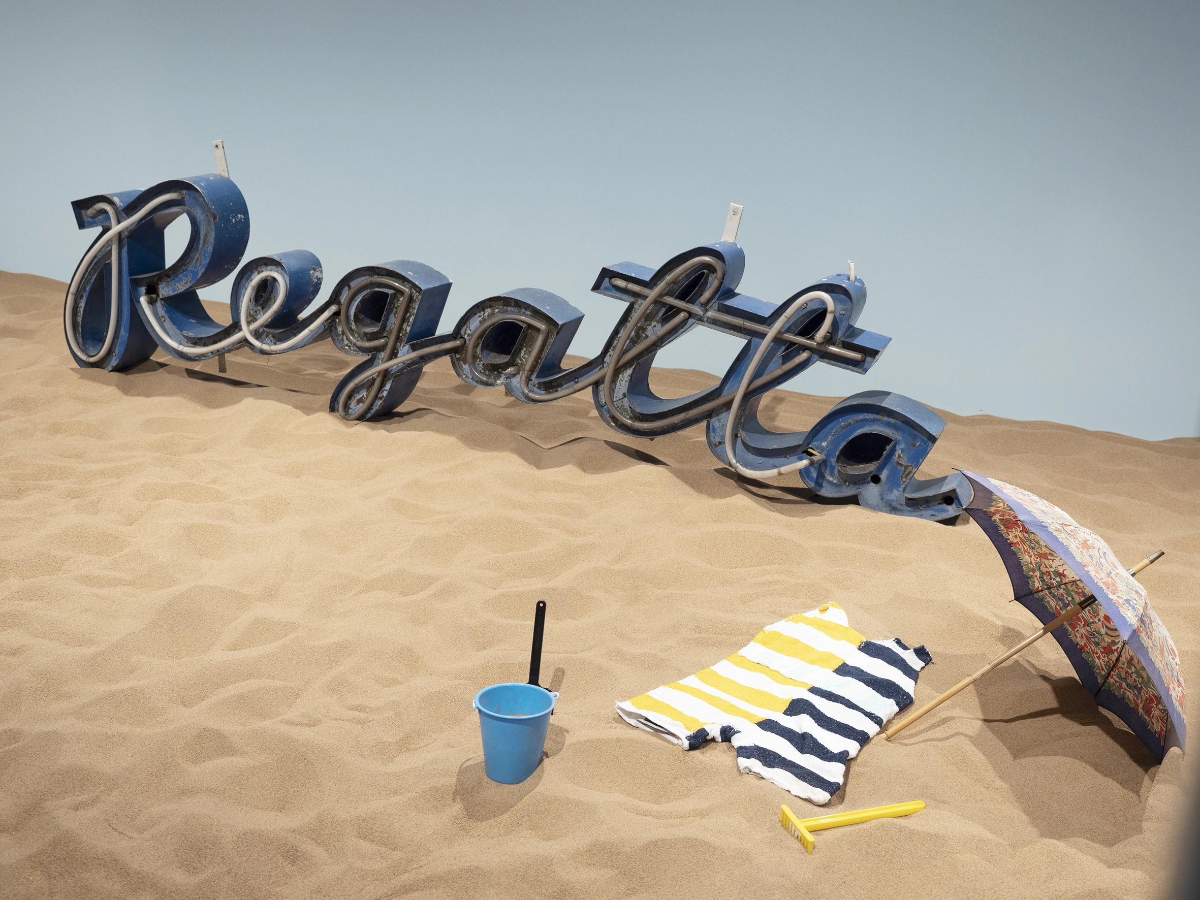 Hiekkaa, hiekkaleluja, uimapuku sekä Regatta-kyltti näyttelyssä.